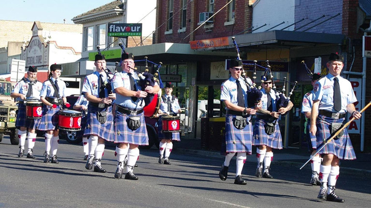 Band members playing the drum and blowing bagpipes as they march down the street.
