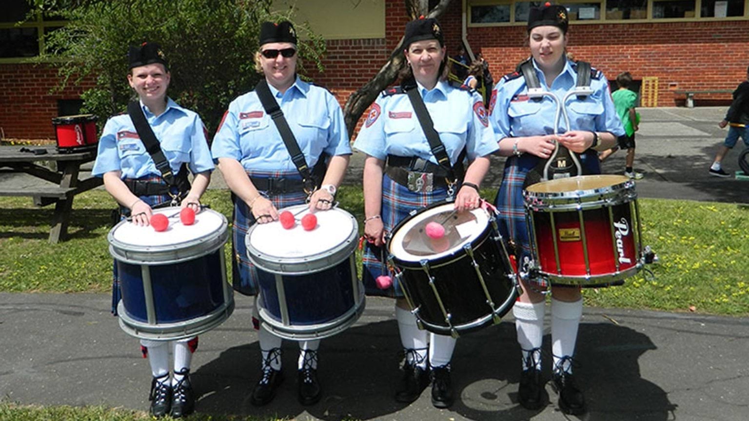 Four female band members are standing in line with their drums.