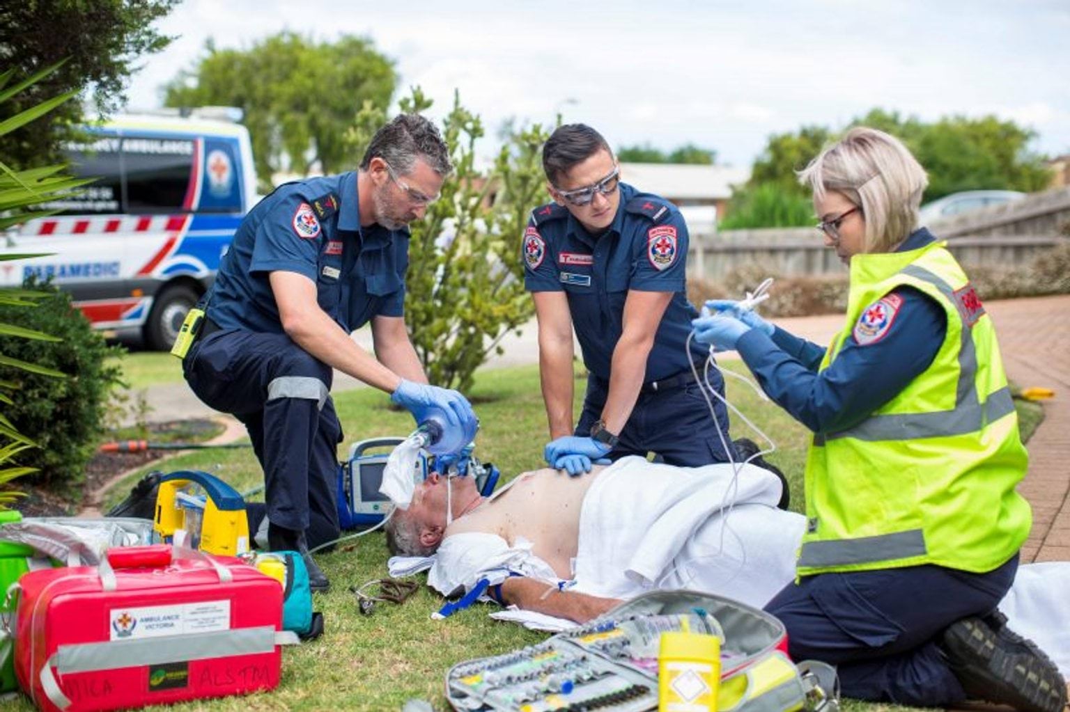 Three paramedics providing life saving help to a person lying on the ground.