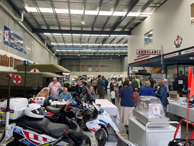 A big garage full of historical ambulance vehicles and equipment. People walk around looking at different things.