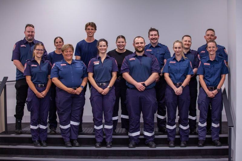 A group of 13 people, most in Ambulance Victoria uniform, smile for the camera.