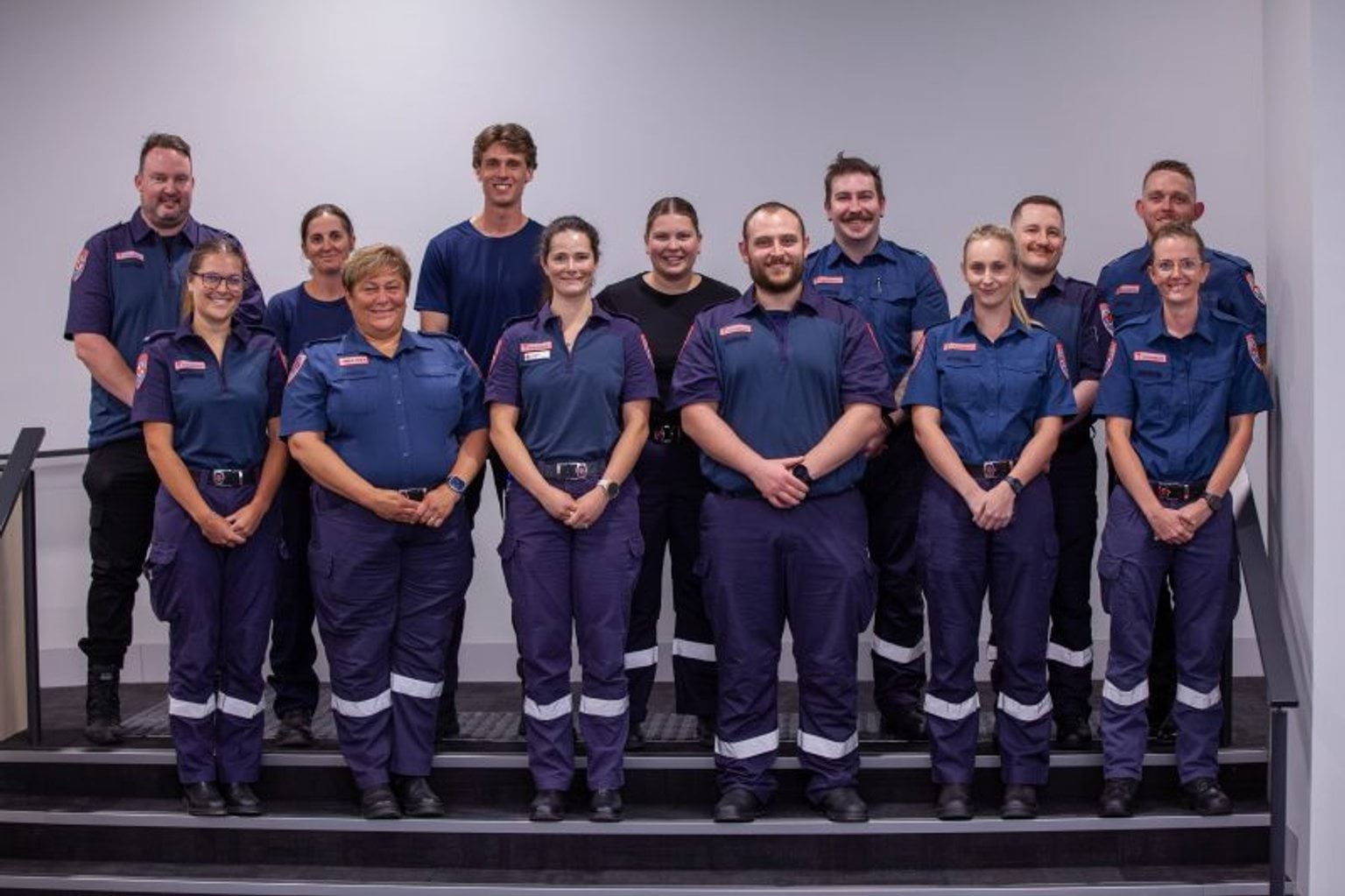 A group of 13 people, most in Ambulance Victoria uniform, smile for the camera.