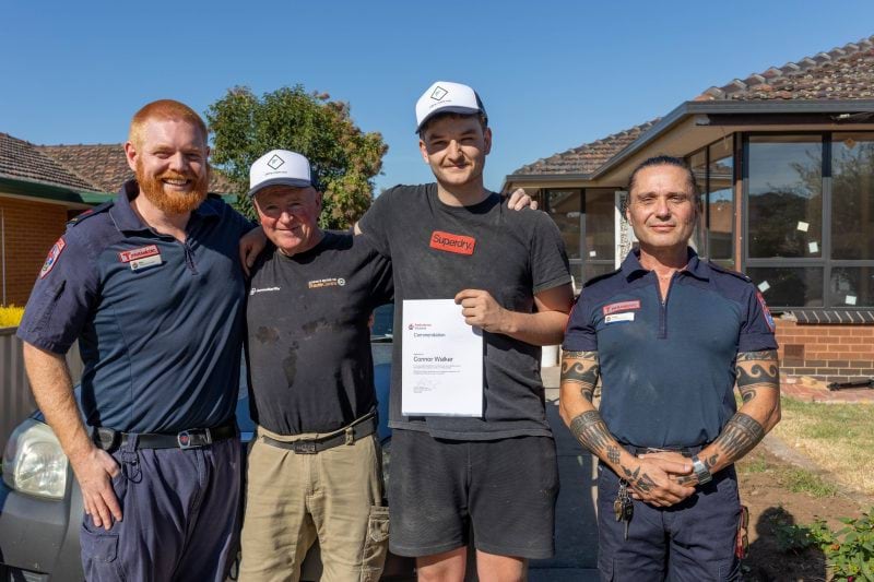 Two paramedics smile for the camera with two tradesmen. One man holds a commendation certificate.