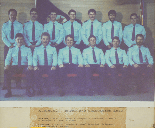 An old photocopied photograph of a group of graduates. The front row are seated on a bench and the back row are standing.