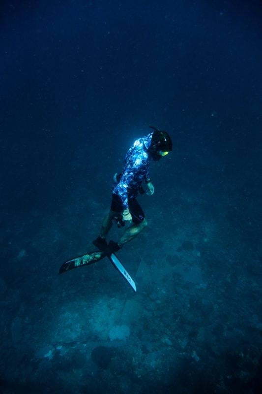 An underwater photo of a person diving. They look like they're floating near the bottom of the ocean.