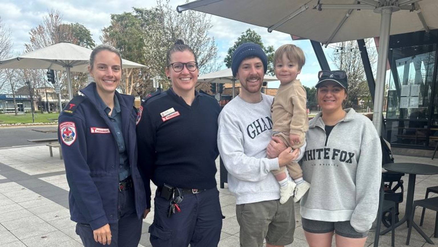 Two female paramedics standing with a young couple and their toddler.