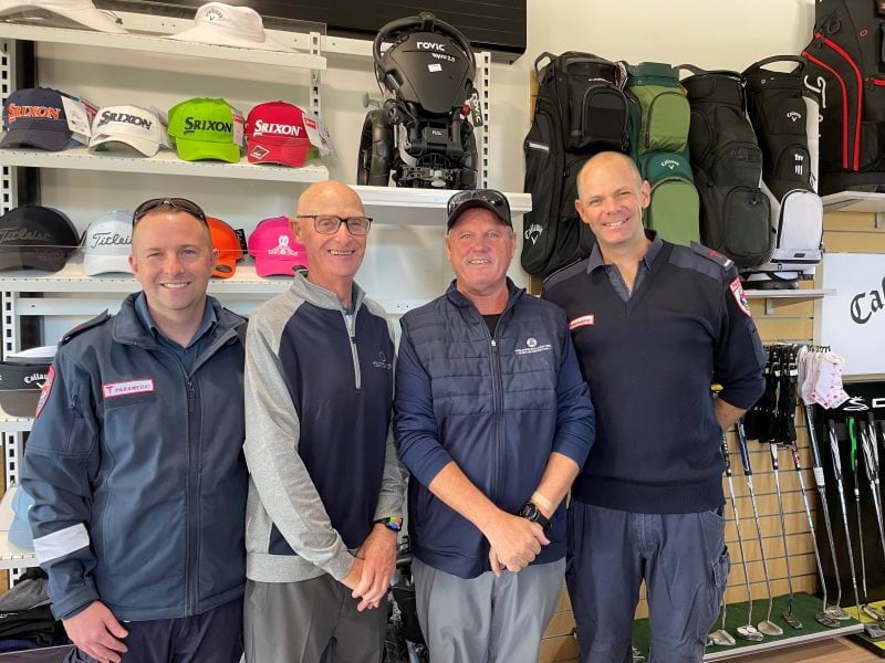 Two paramedics and two men in casual clothes smile for the camera. Golf equipment is behind them.