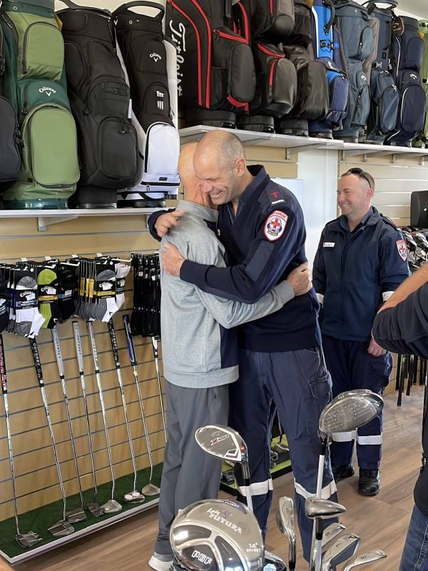 A paramedic hugs a man in casual clothes inside a golf shop.