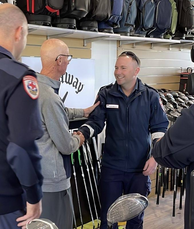 A paramedic shakes hands with a man in a grey jumper. They're in a golf shop.