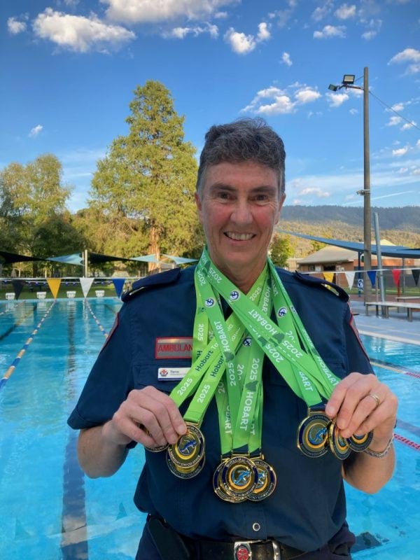 A woman in a paramedic uniform with 12 medals around her neck, standing in front of a pool.