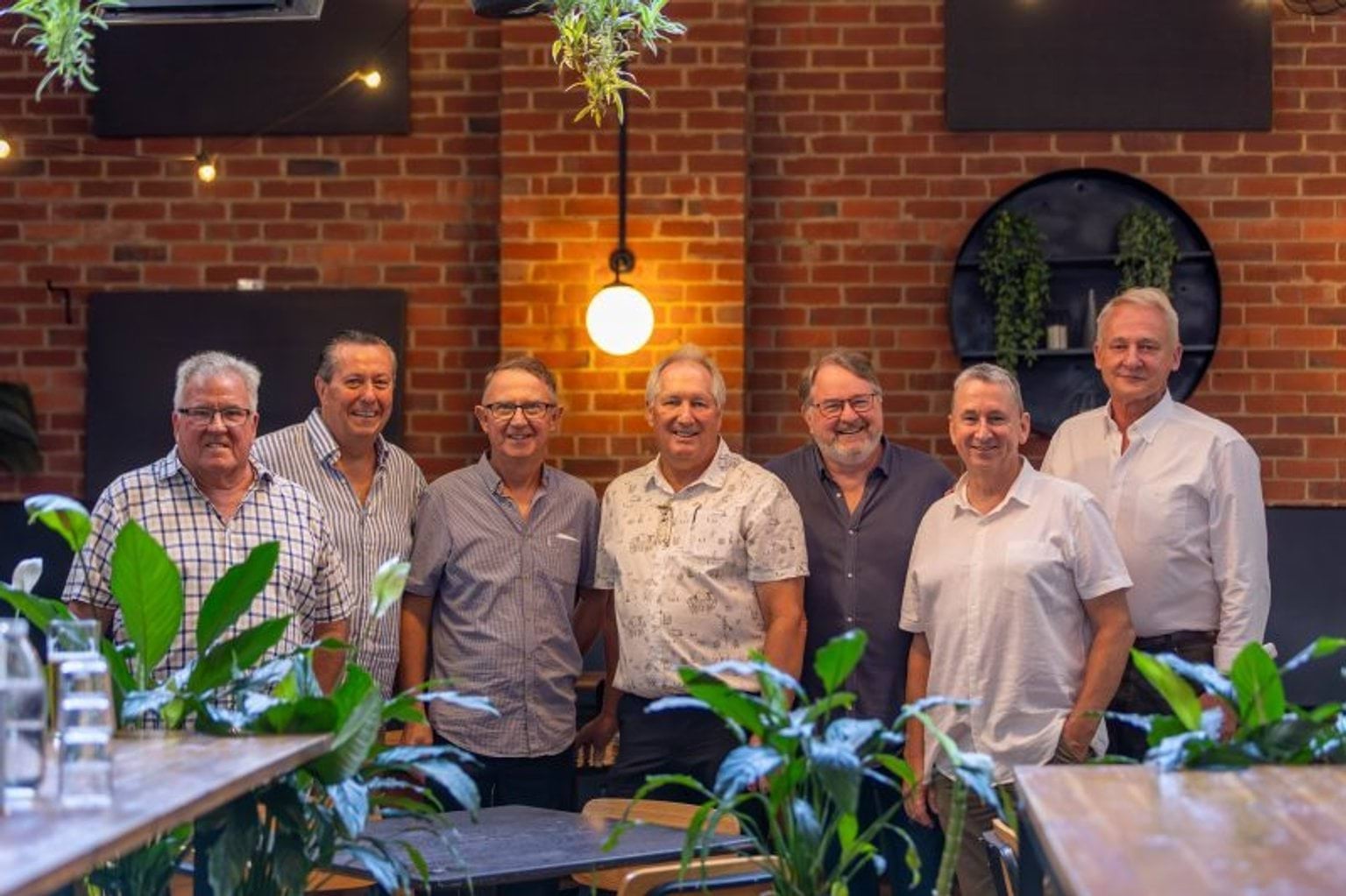 Seven men stand together in a restaurant