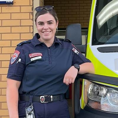 A female paramedic leaning against an ambulance.