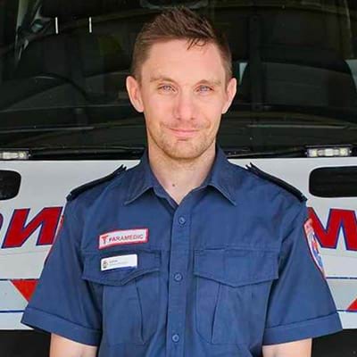 A male paramedic standing in front of an ambulance.