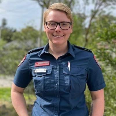 A female paramedic smiling while standing in a garden.
