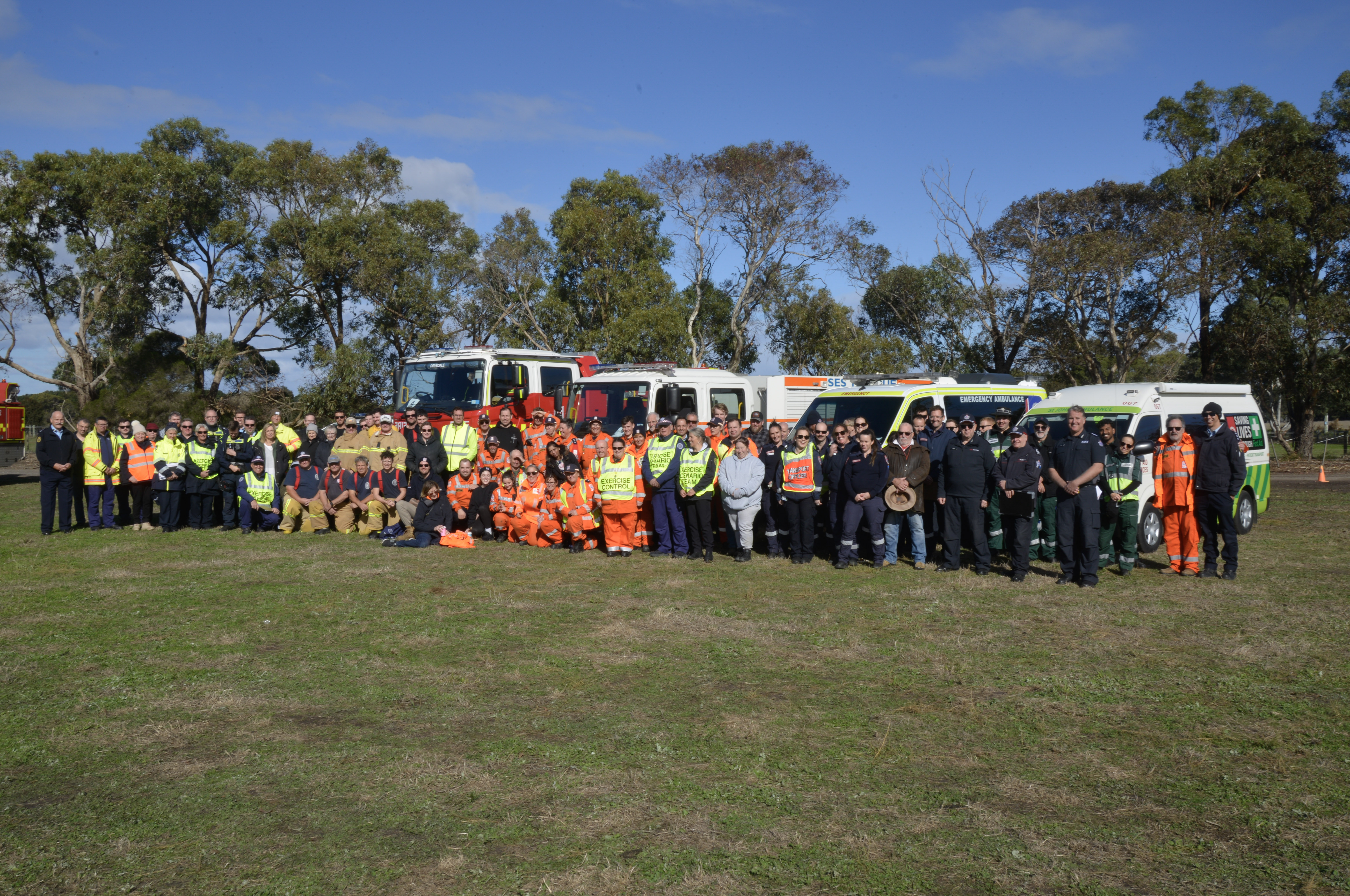 A large group of emergency service personnel pose for the camera in front of emergency service vehicles.