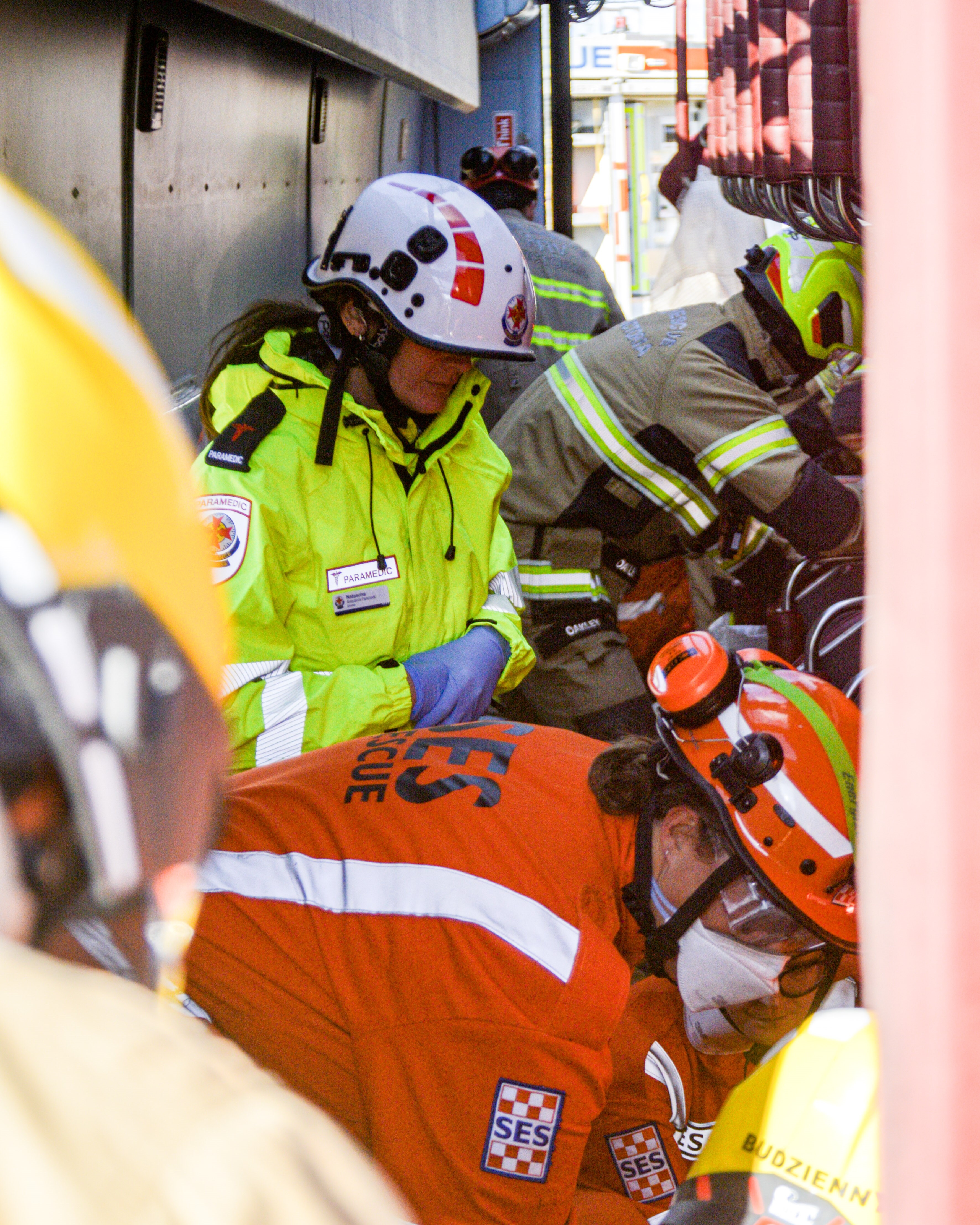 A paramedic, SES volunteers and firefighters work inside a bus that has tipped on its side.