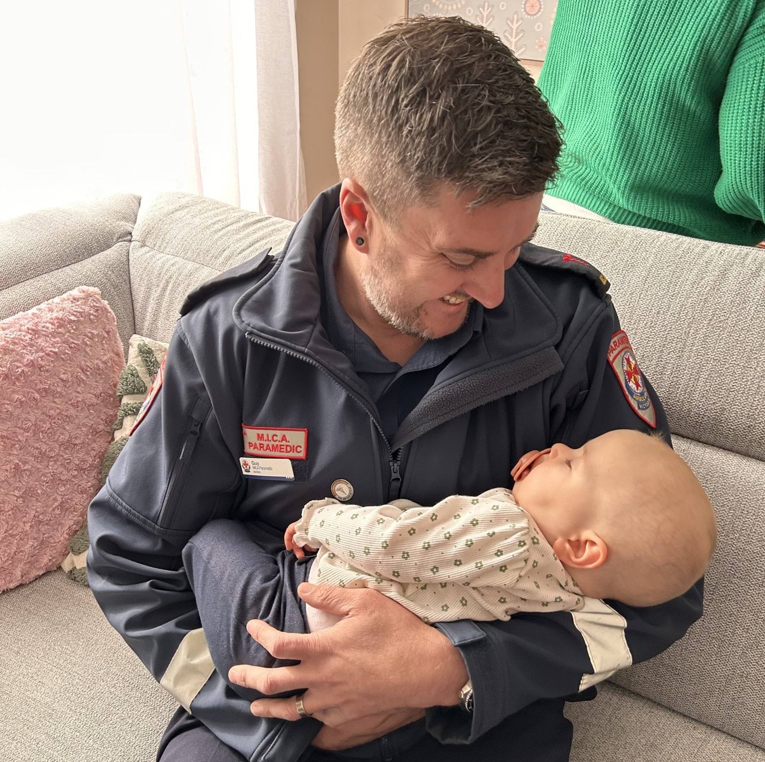 A male paramedic smiling while holding a one year old baby.
