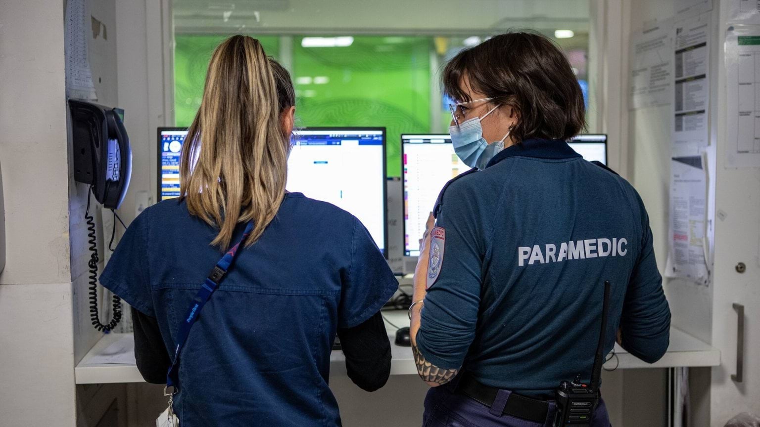 A paramedic stands with a nurse. They have their backs to the camera.
