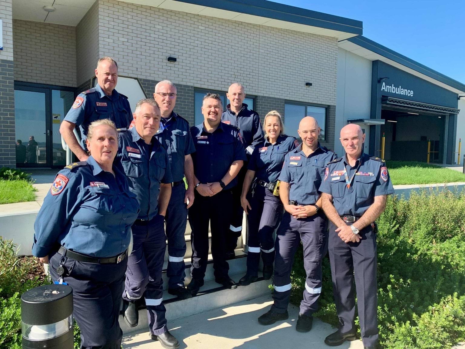 A group of nine people wearing paramedic uniforms in front of a building.