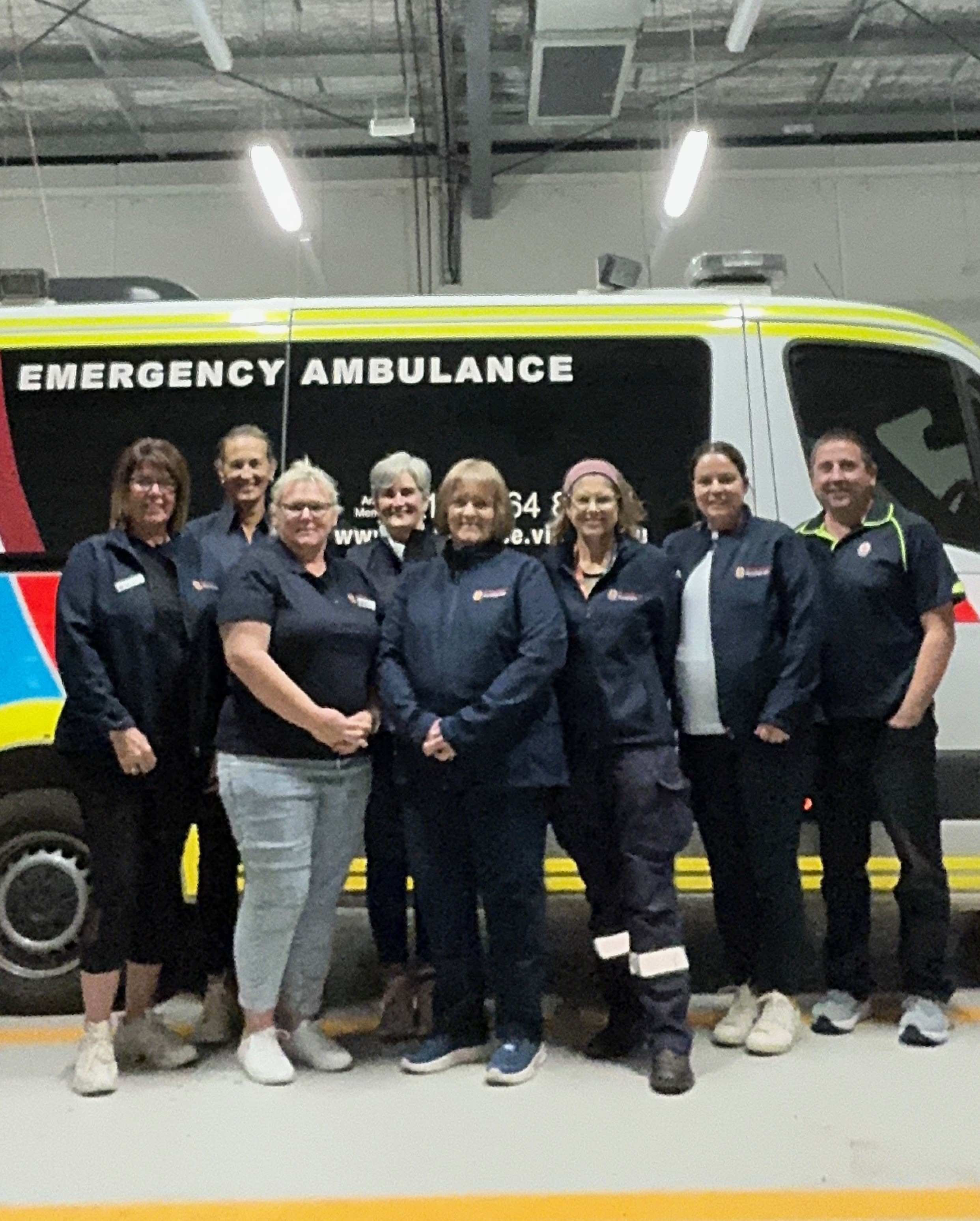 A group of eight people standing in front of an ambulance.