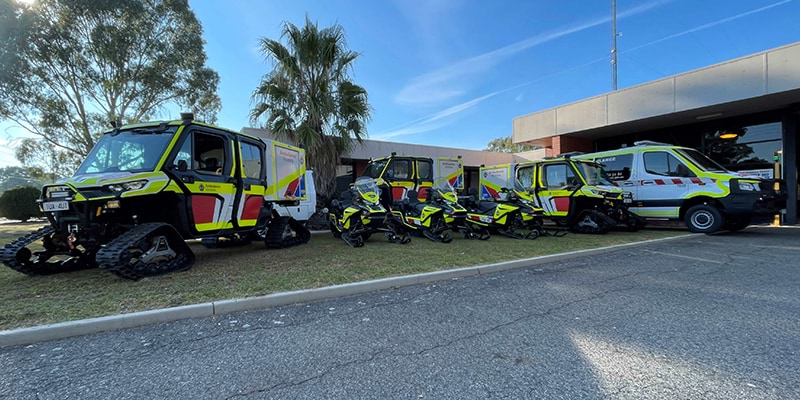 Emergency vehicles, including several snow vehicles, are parked outside a building, prepared for quick deployment in case of emergencies.
