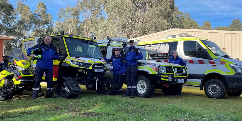 Three people standing next to four emergency vehicles, ready to provide emergency medical assistance.