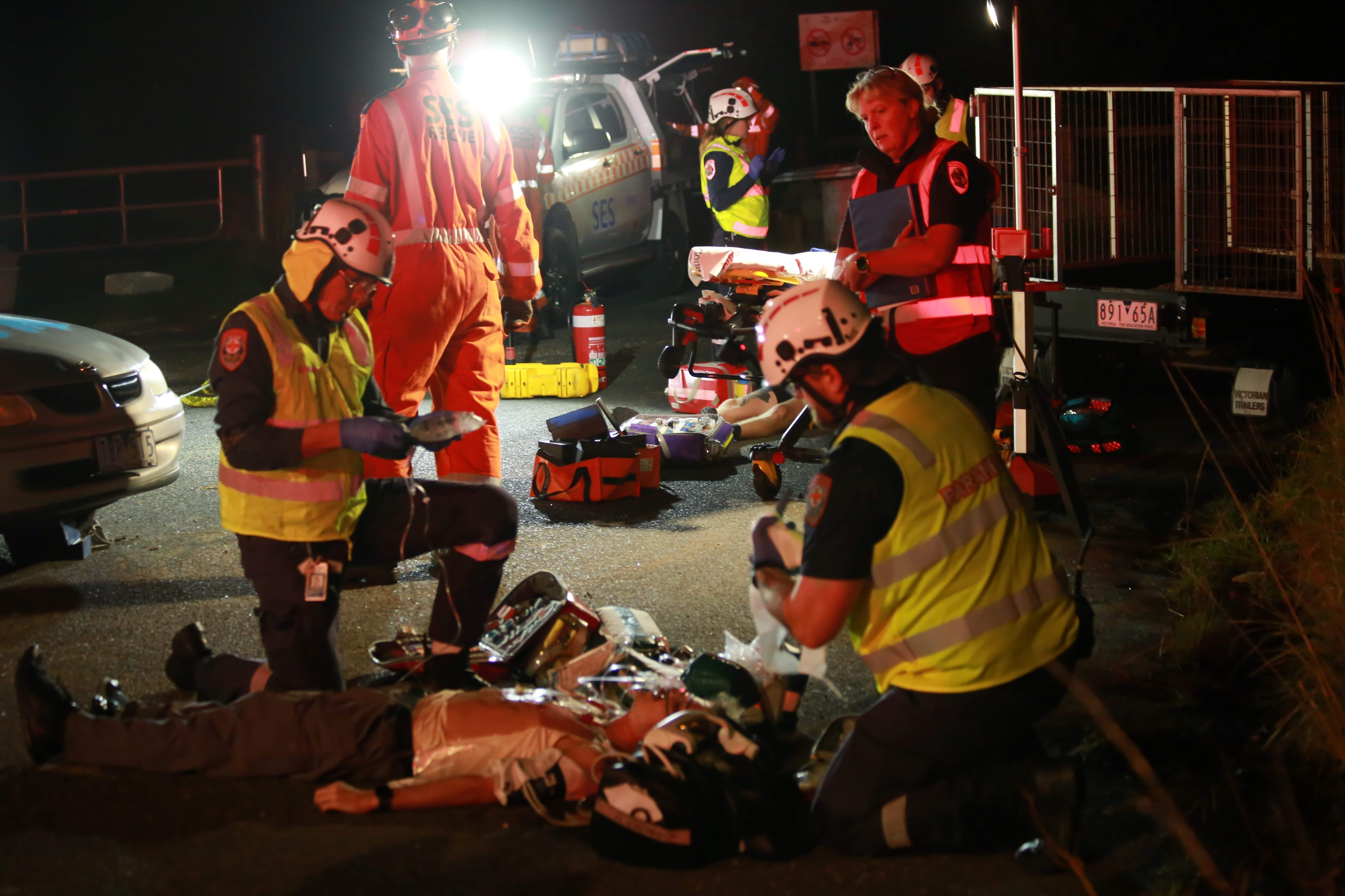 Two paramedics are being observed as they treat a person lying on the road.