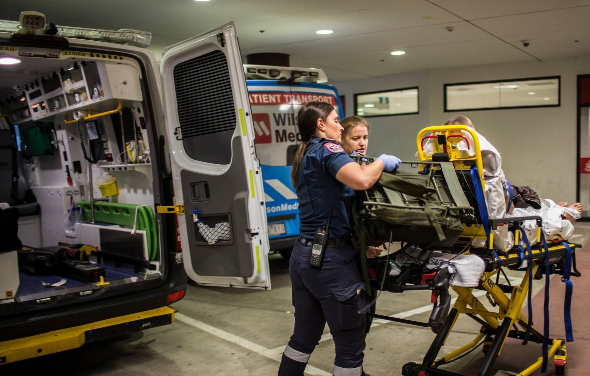 Two paramedics wheel a patient on a stretcher towards a hospital.