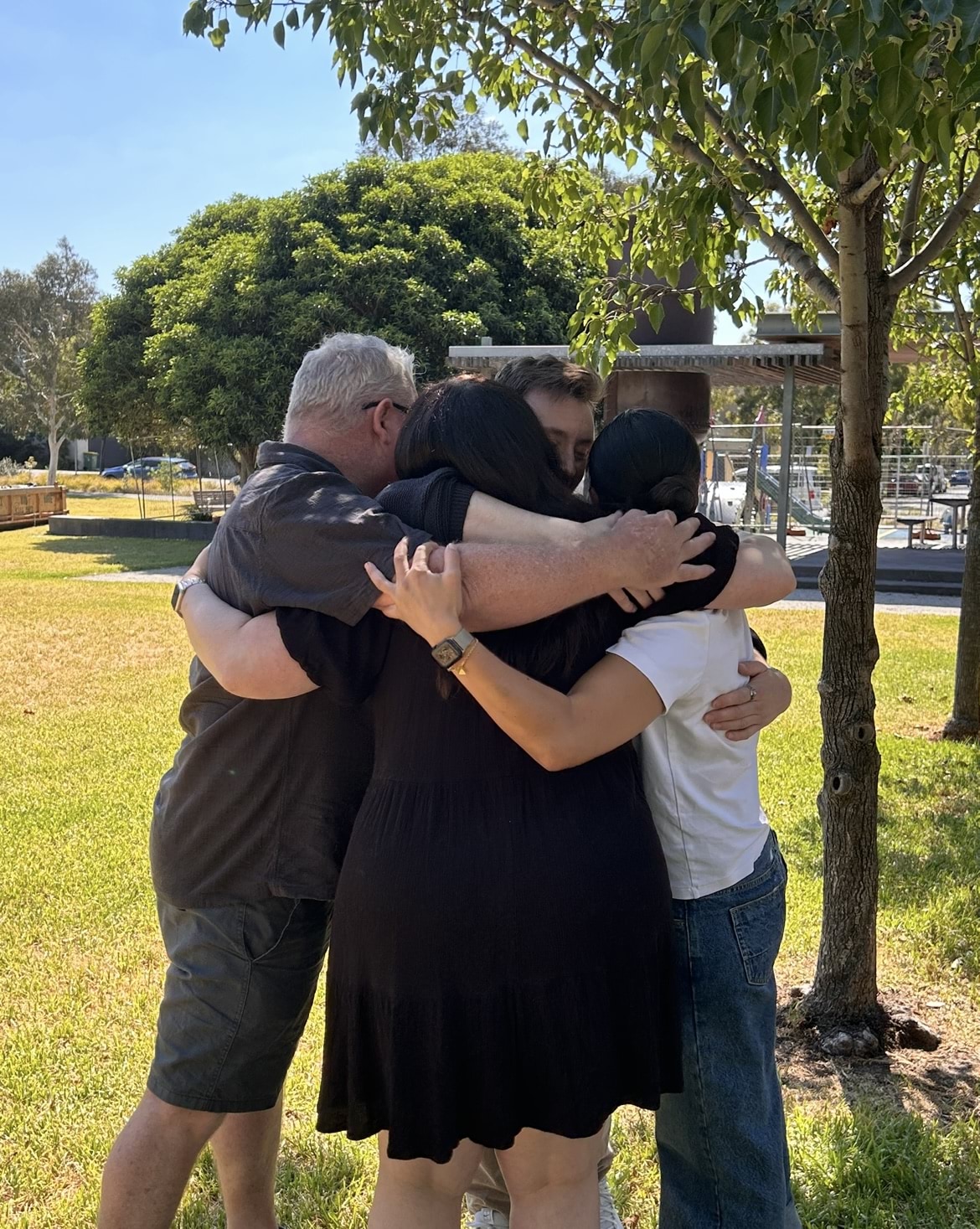 Four people hug in a park on a sunny day.