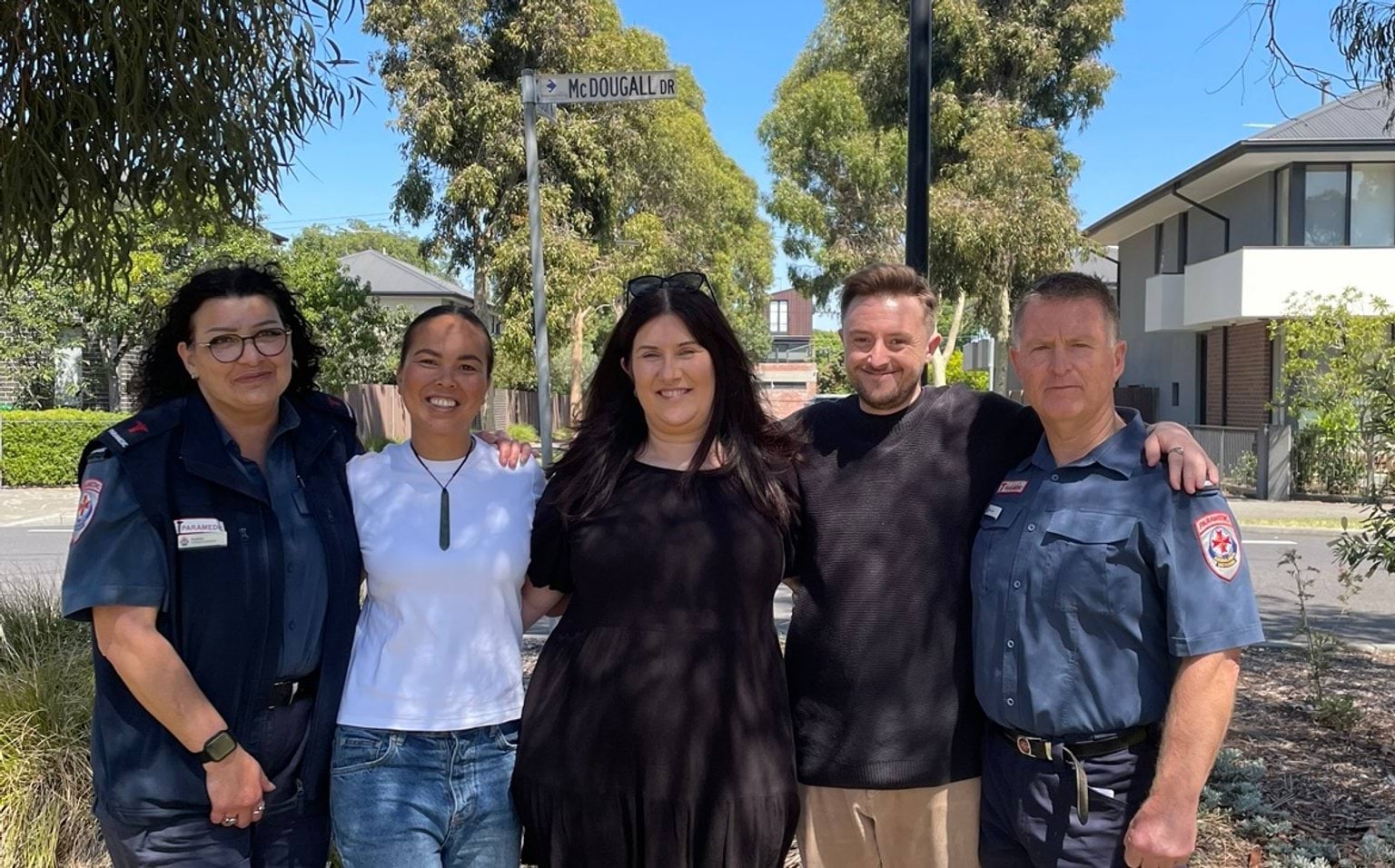 Two paramedics and three people in casual clothes smile for the camera.