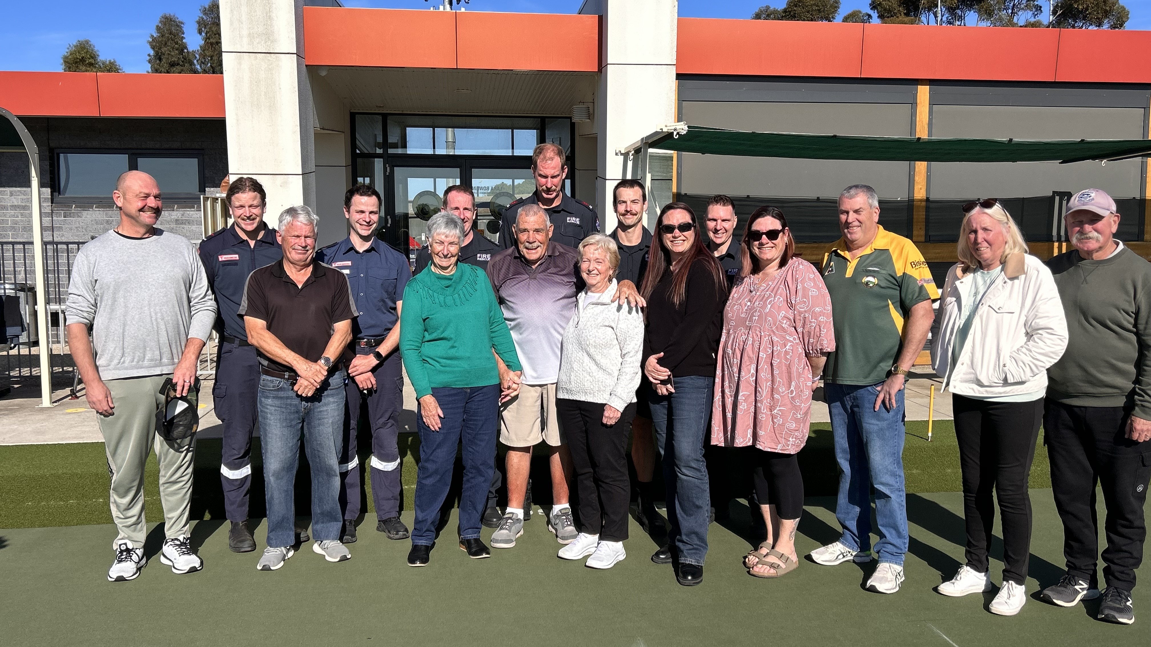 A group of smiling people standing on a lawn bowls green.
