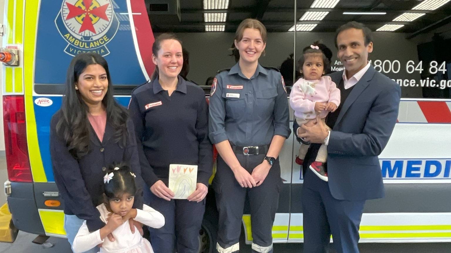 A mother and father with their two daughters, standing either side of two female paramedics.
