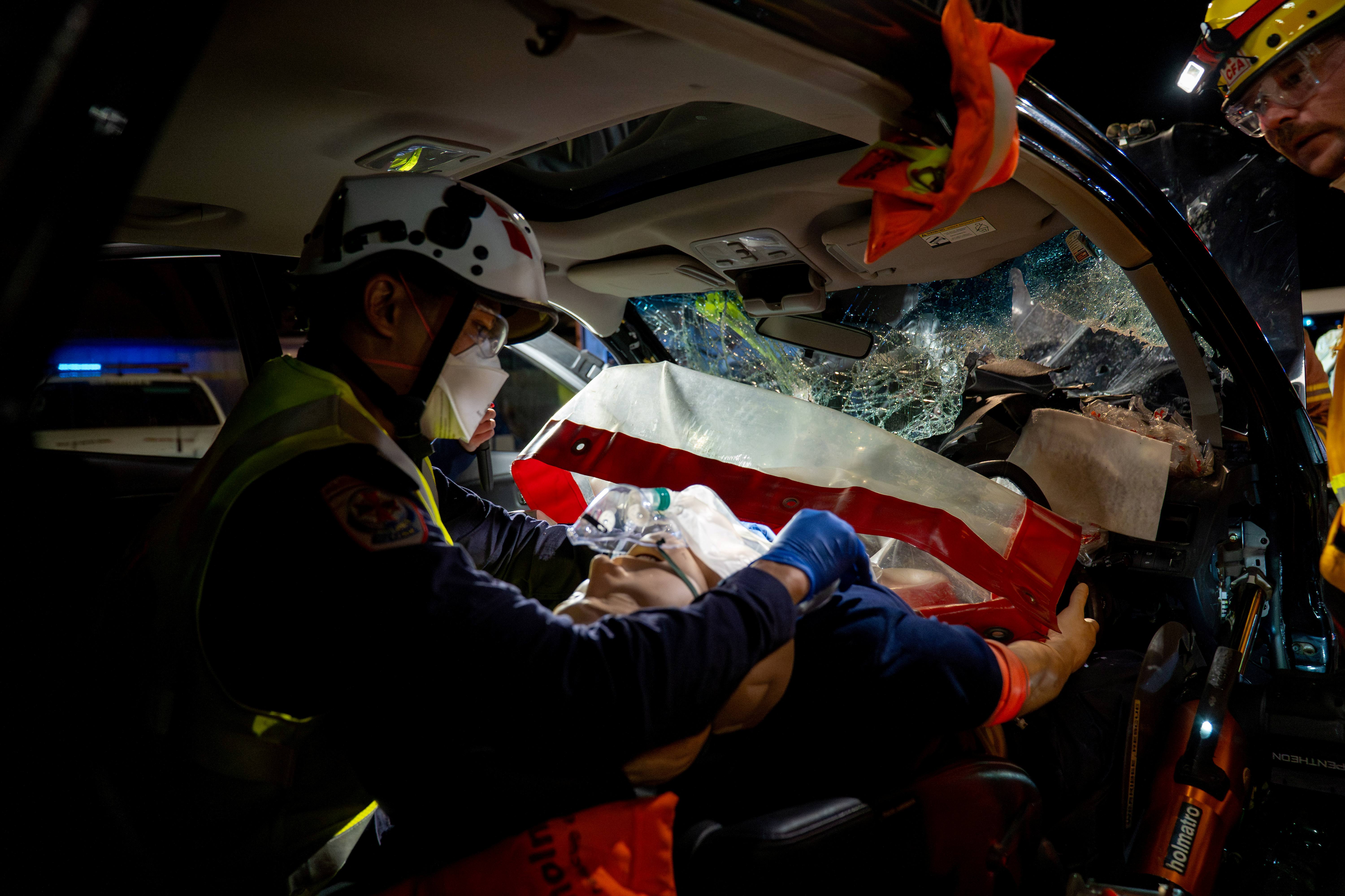 A paramedic treats a mannequin inside a car with a smashed windscreen.