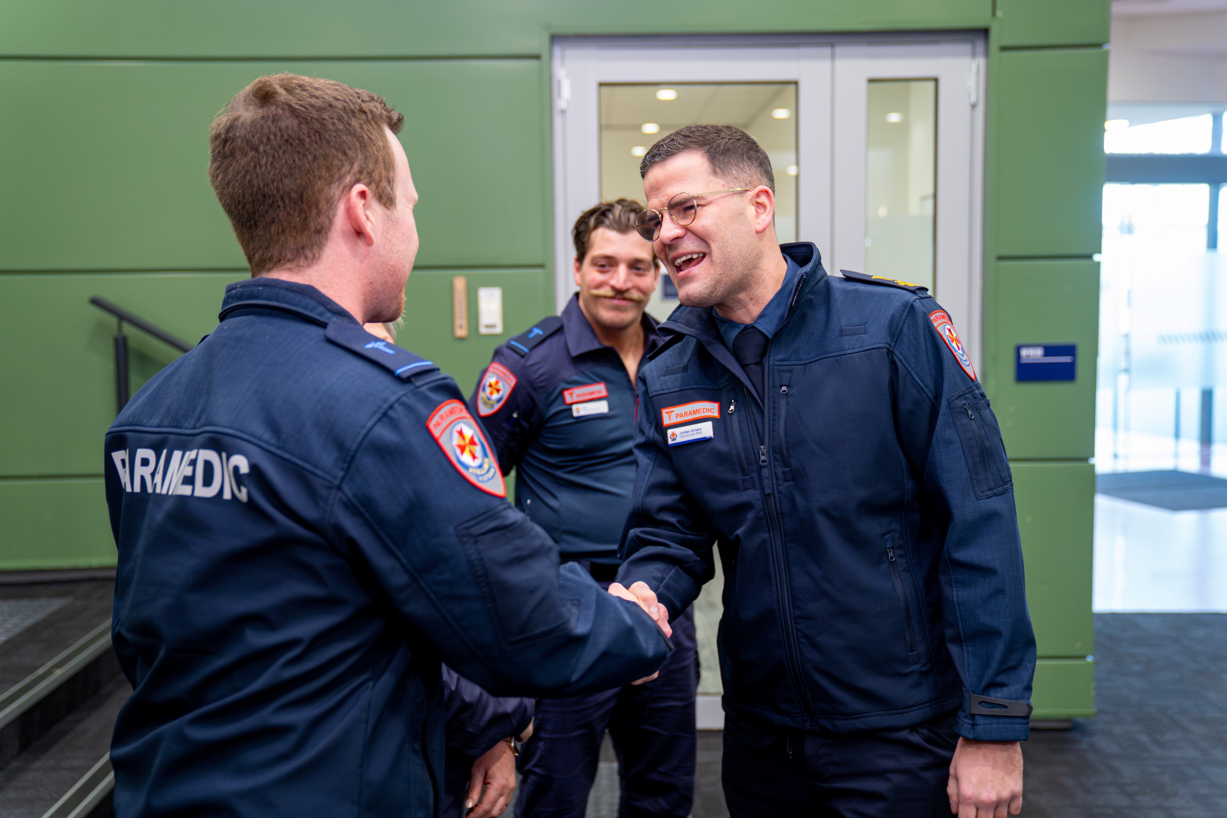Two men in paramedic uniform shake hands.