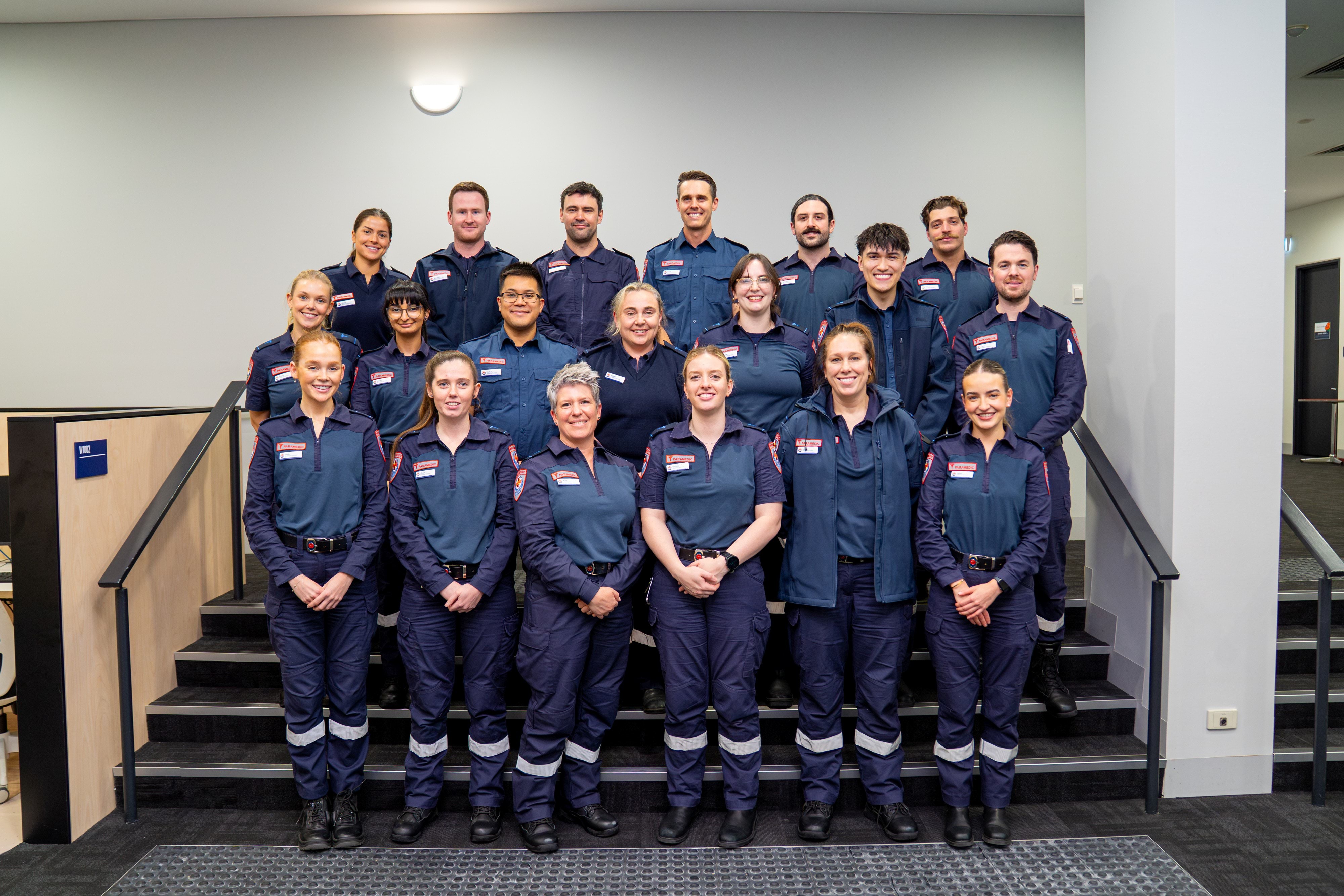A group of paramedics smile for the camera. They are posed on a set of stairs.