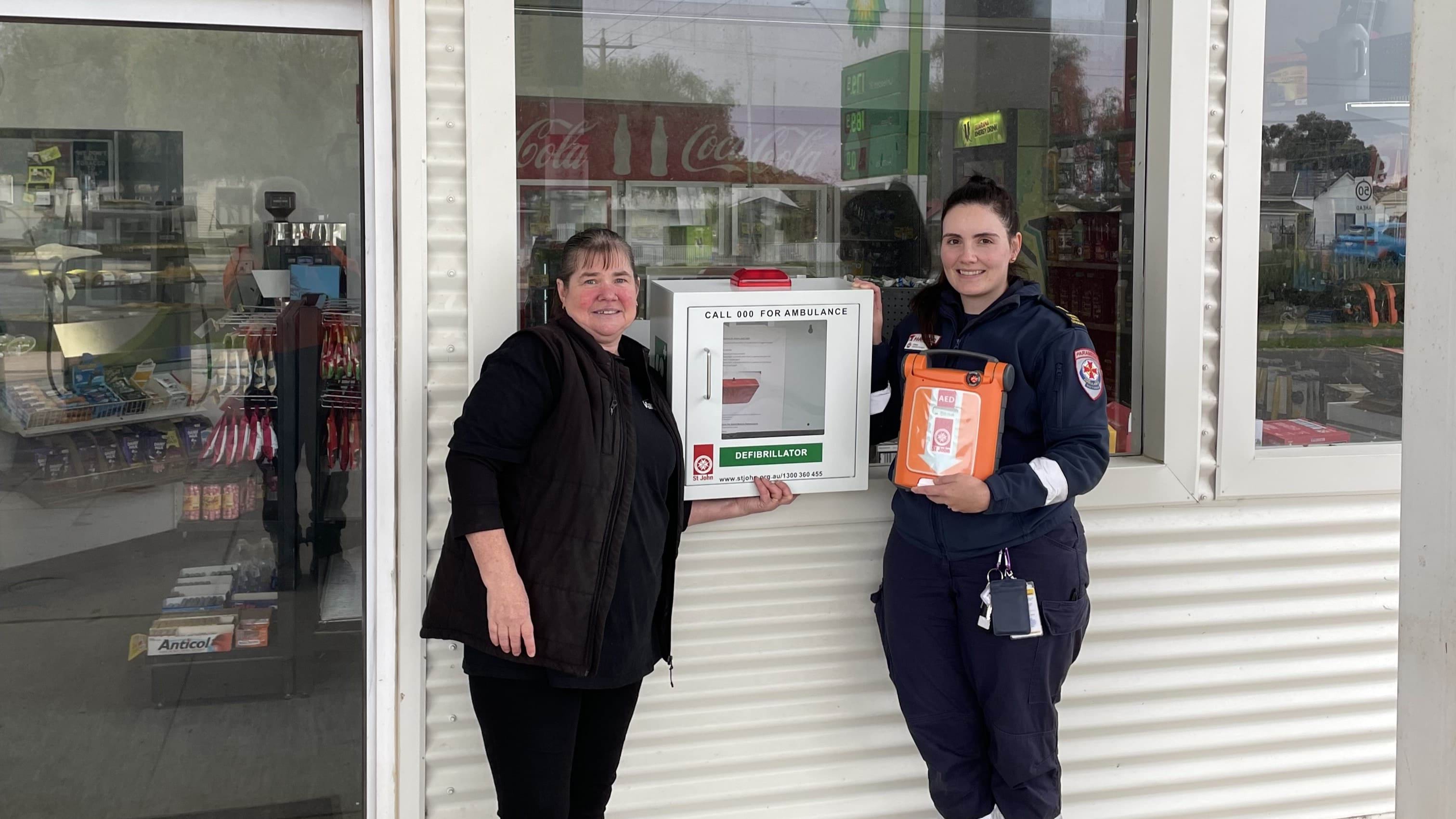 Two smiling woman, one is holding an automated external defibrillator (AED).