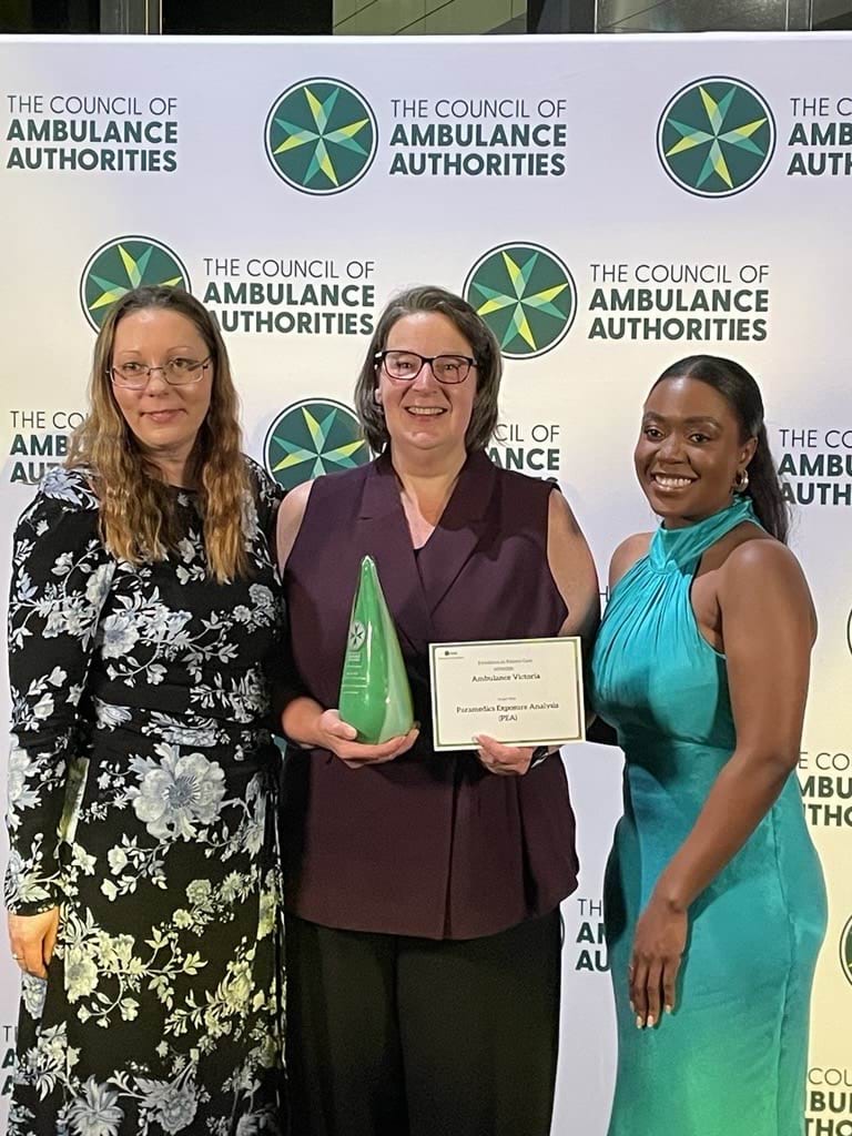 Three women smile for the camera holding an award trophy and a certificate.