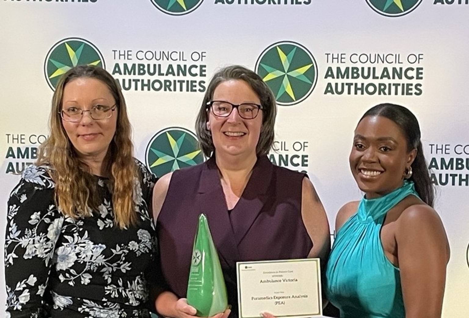Three women smile for the camera holding an award trophy and a certificate.