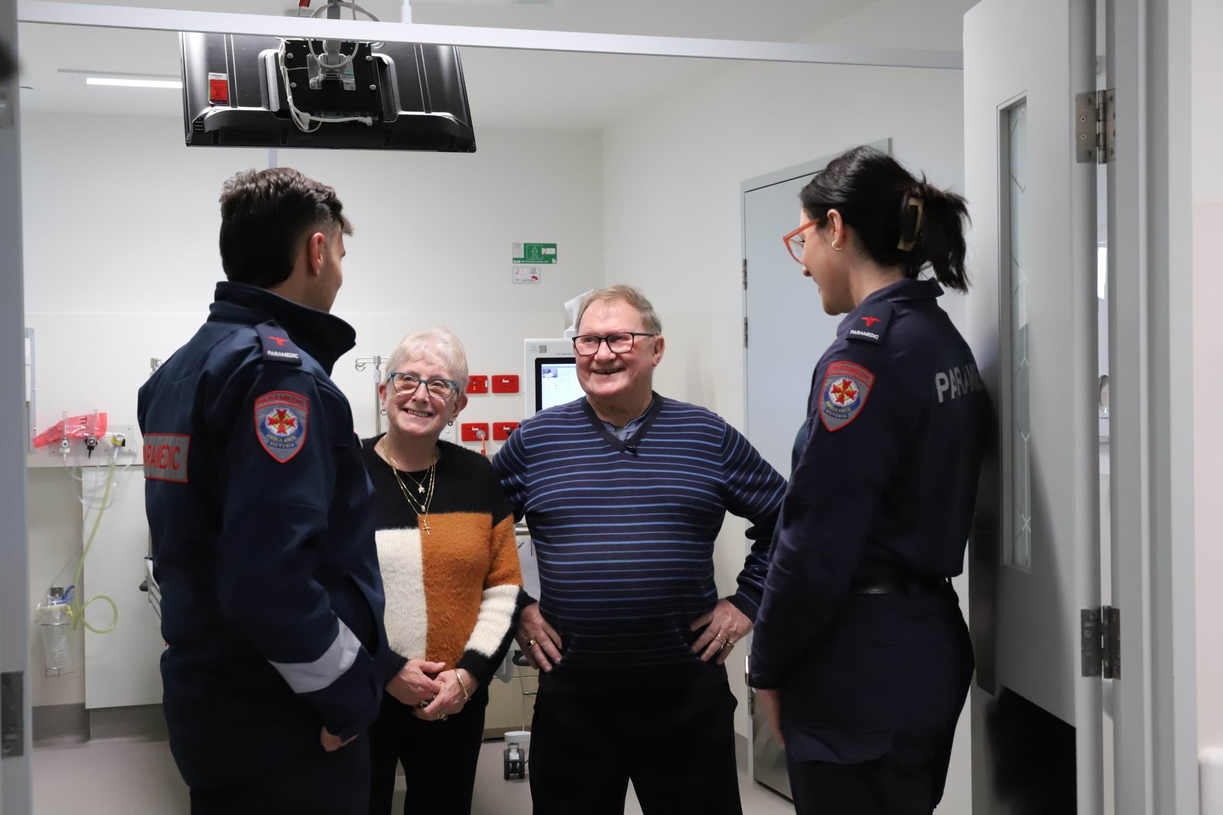 A man and woman in casual clothes speak to two paramedics in a hospital ward.