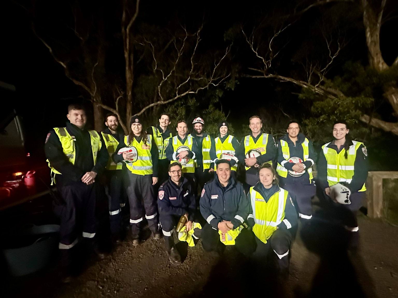 A group of people in Ambulance Victoria uniform, in a park at night.