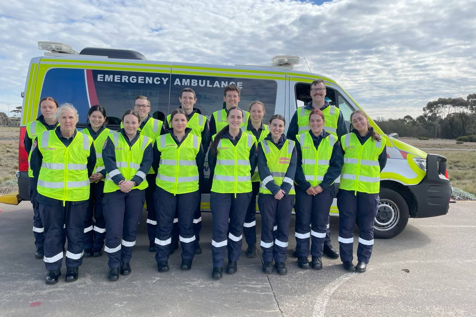 A group of Ambulance Victoria paramedics smile for the camera in high-vis yellow vests.