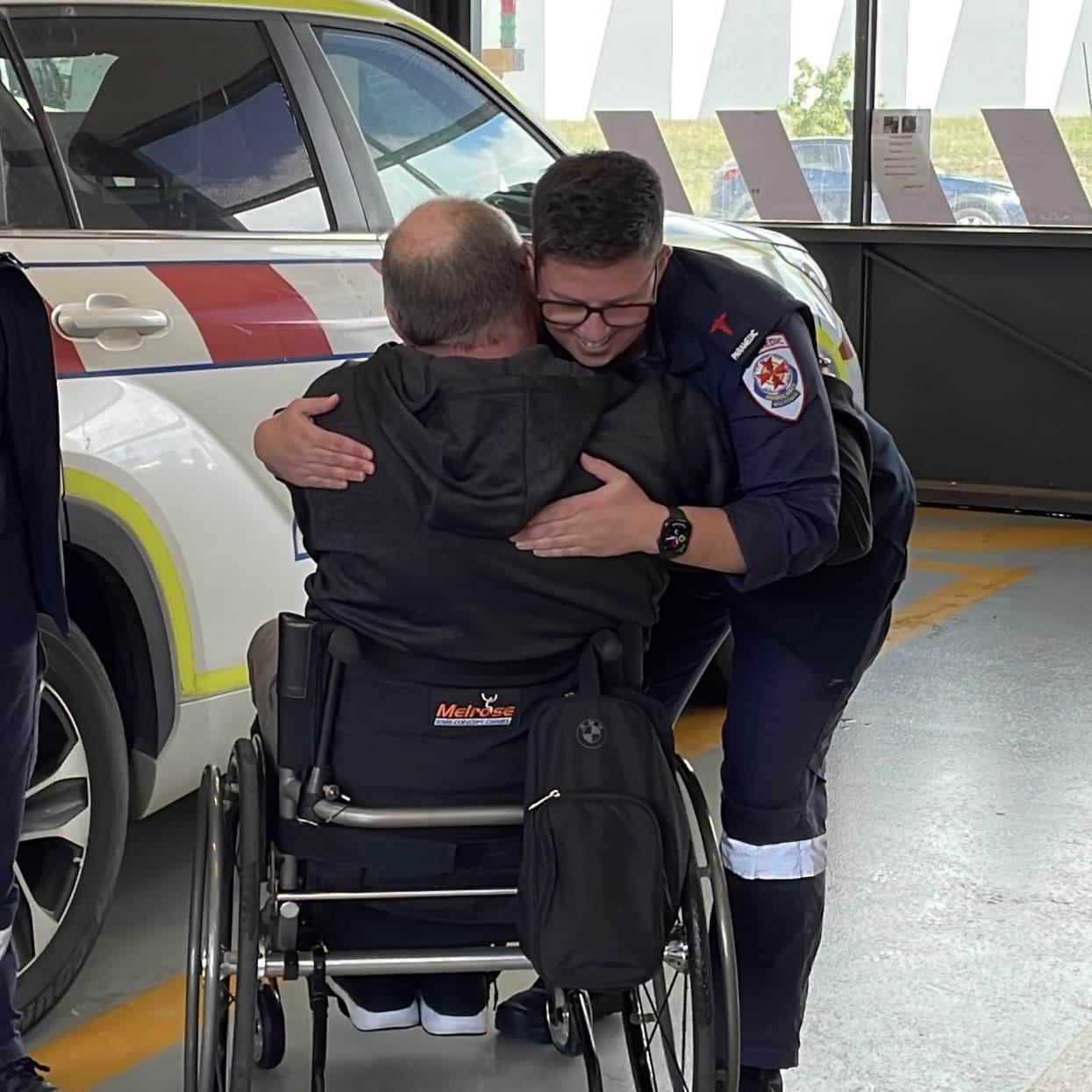 A paramedic hugs a man in a wheelchair.