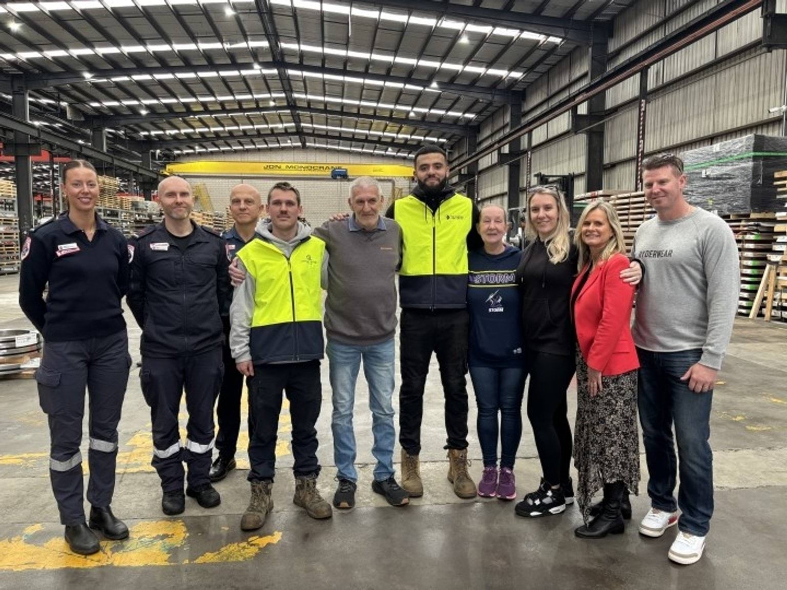 A group of paramedics, workers and family pose for a group photo in a factory.