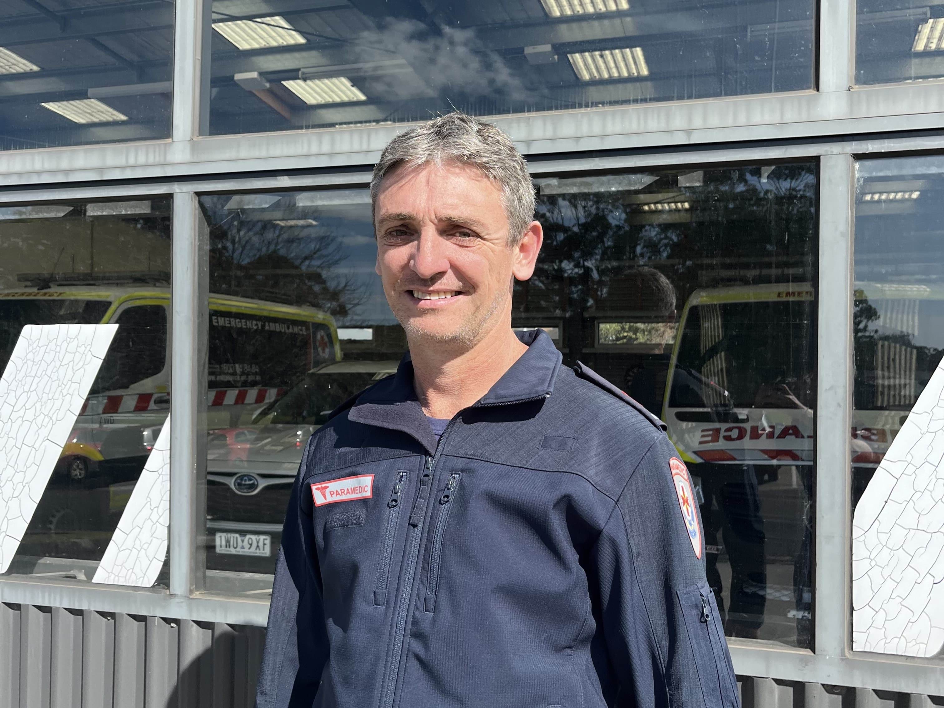 A headshot of an Ambulance Victoria paramedic. He is standing in front of a garage.