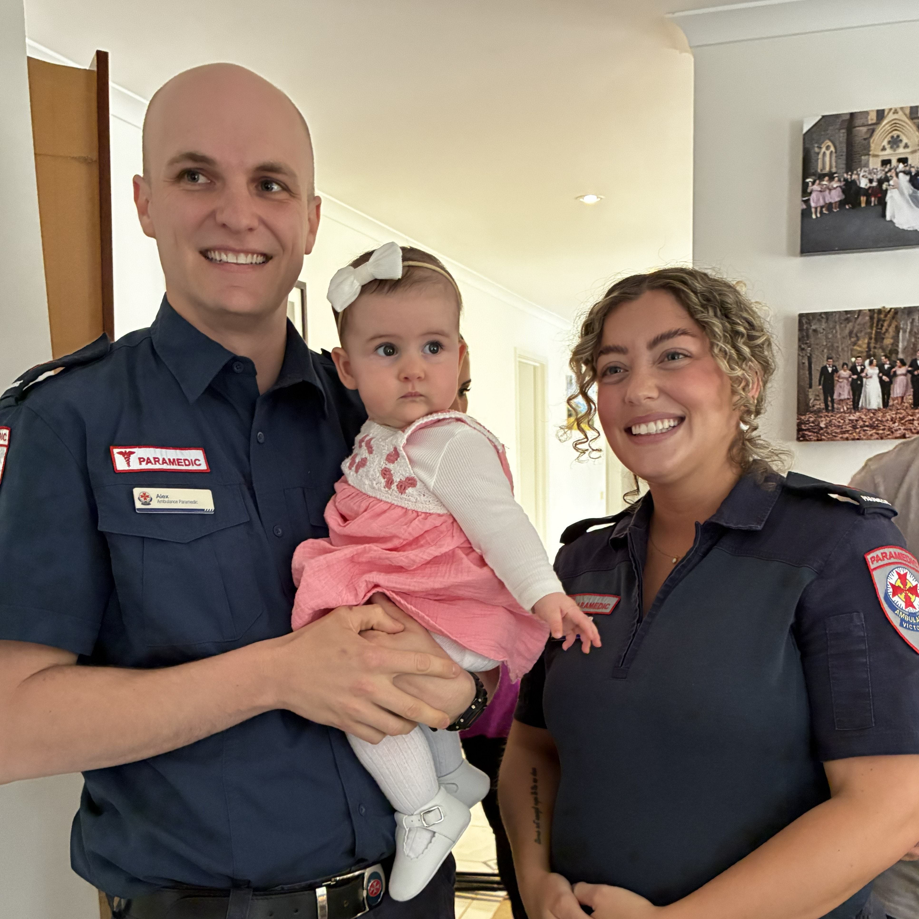 Two paramedics smile while one holds a very young girl.