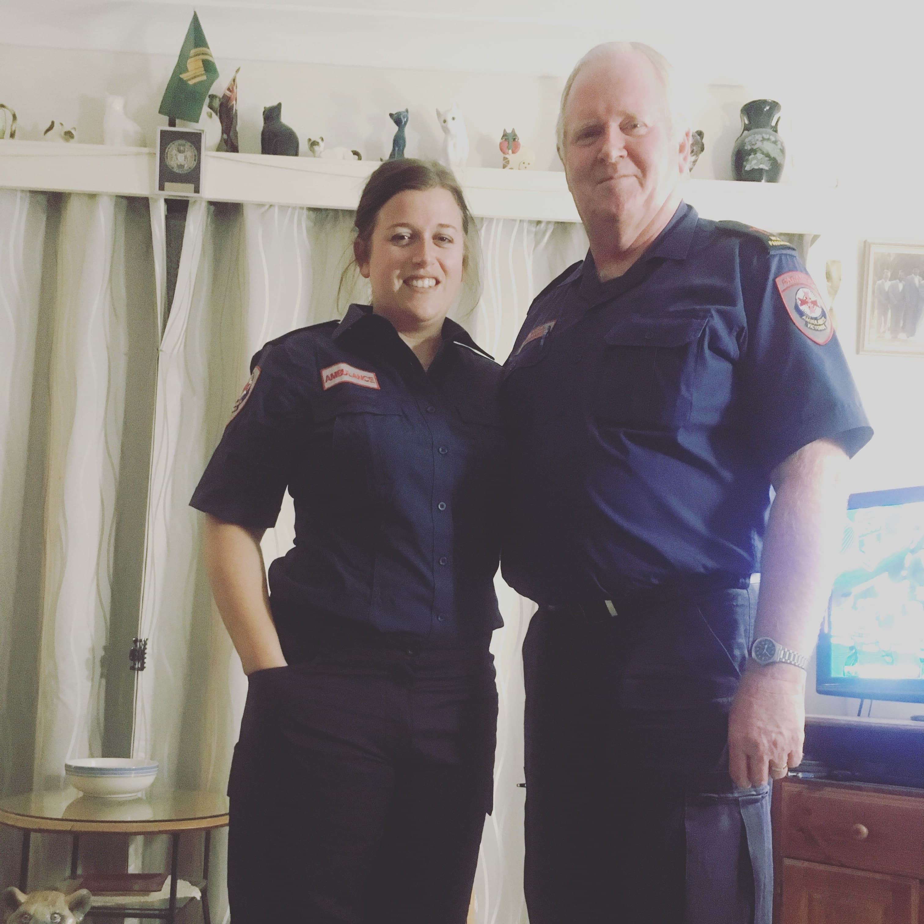 A woman and man in Ambulance Victoria uniform smile for the camera in a living room.