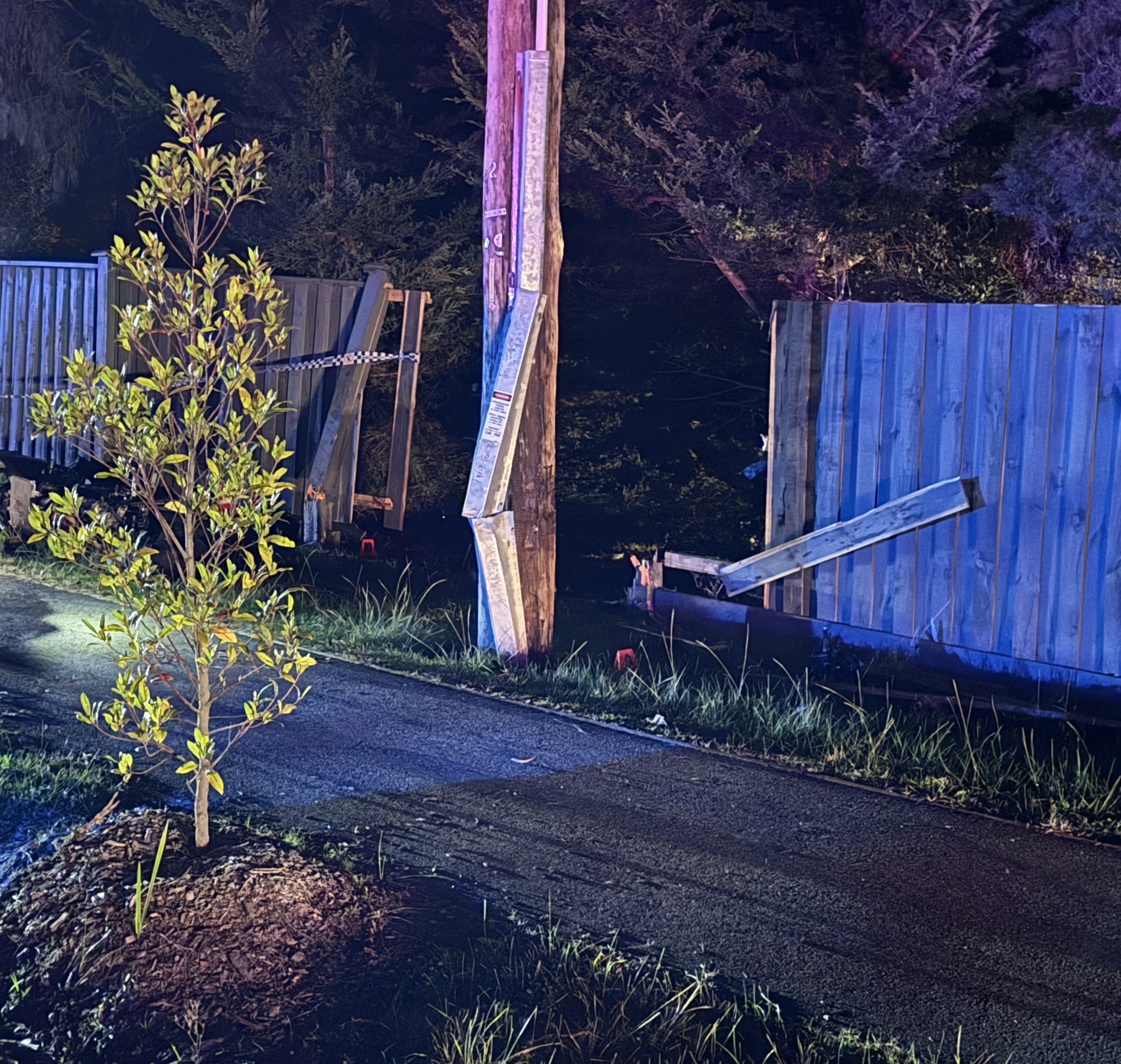 A destroyed wooden fence and an electrical pole with bent metal. It is night time.