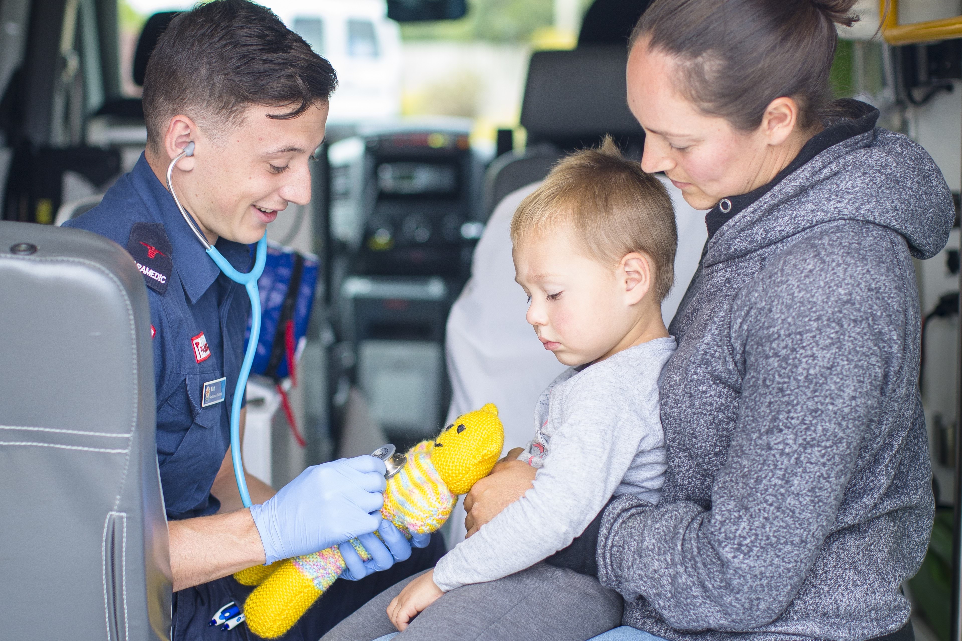 A child and mother sit with a paramedic in an ambulance.