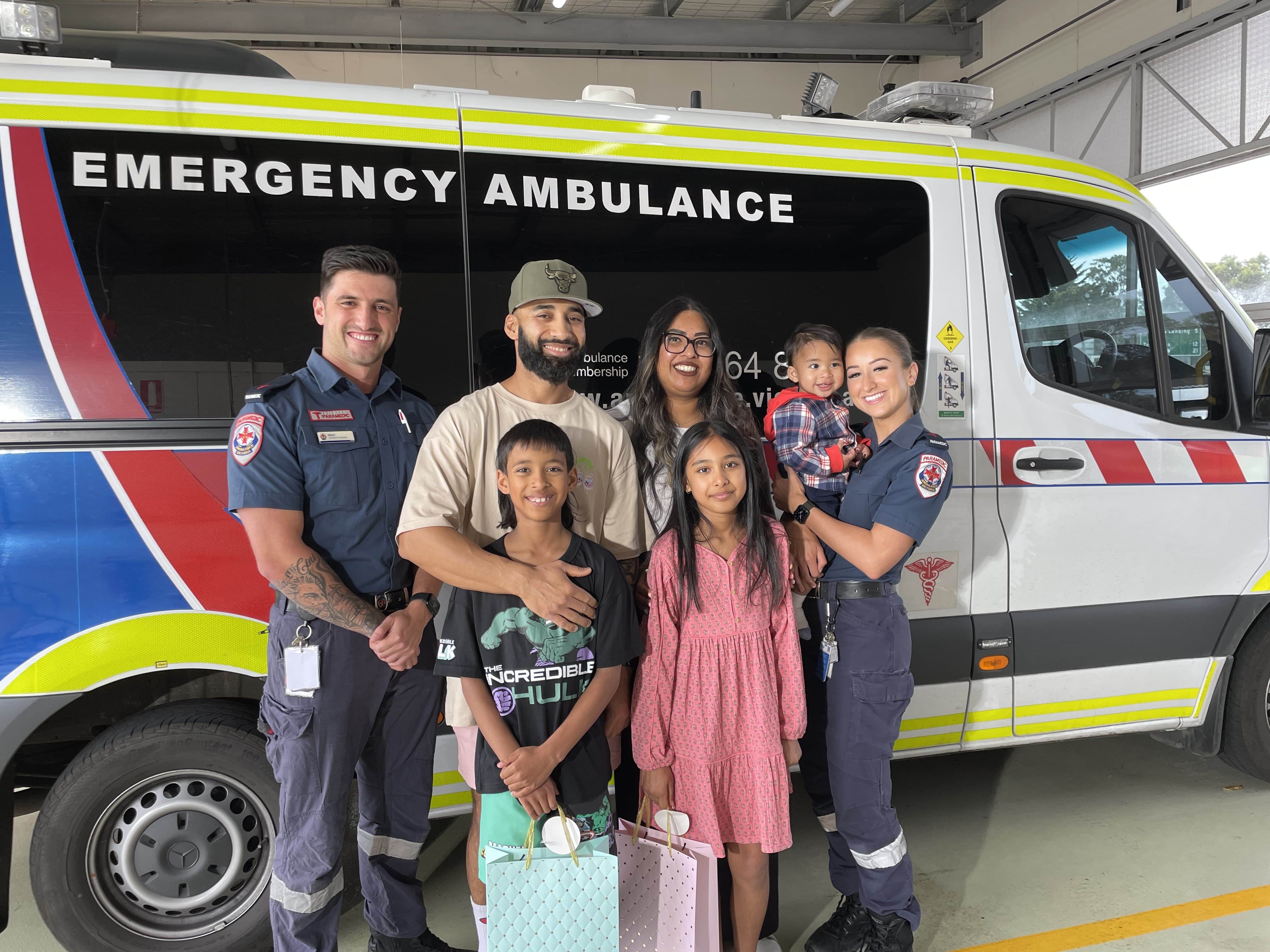 Two paramedics and a family of five smile in front of an ambulance.