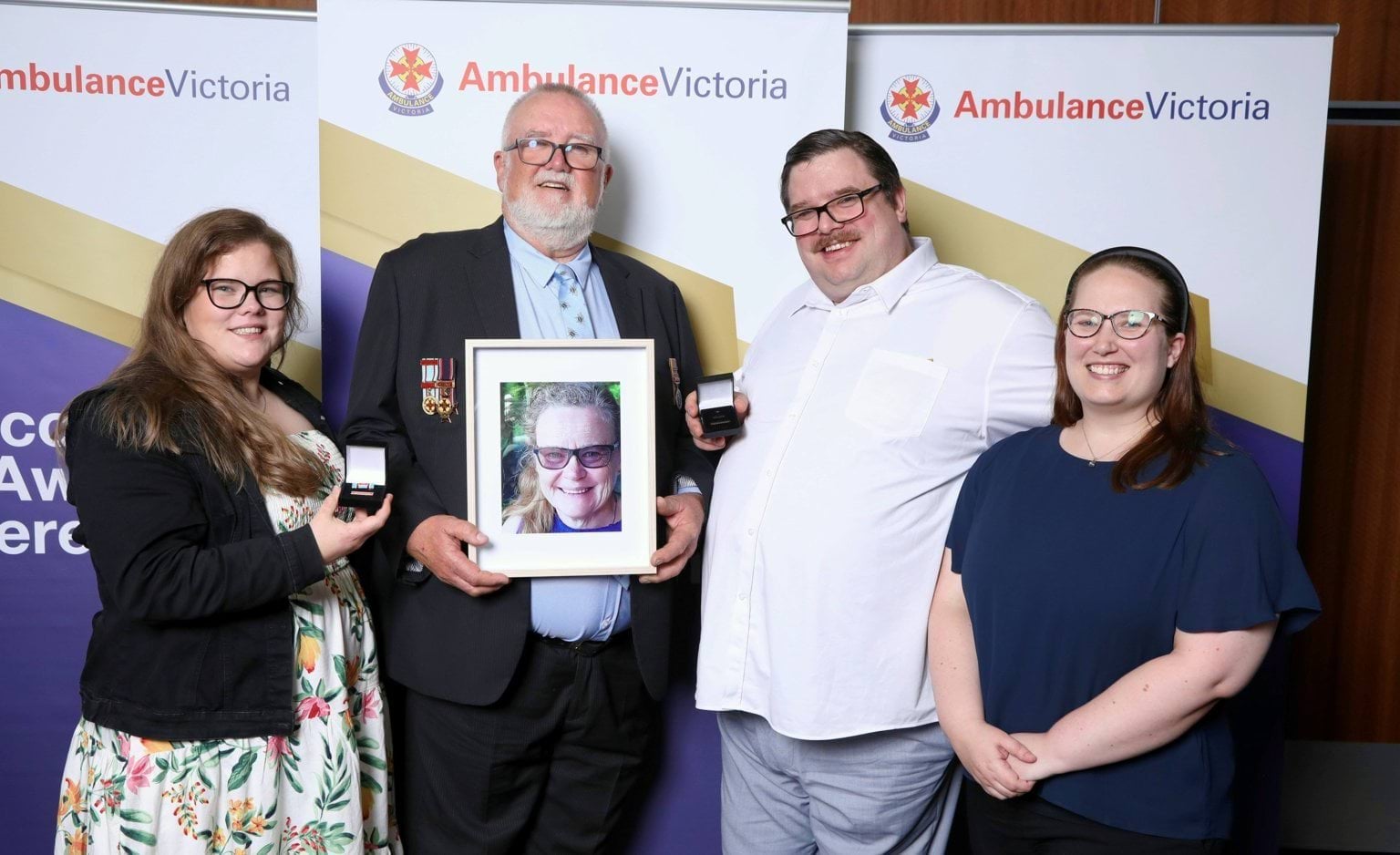 Two men and two women. The oldest man holds a framed photograph of a woman.
